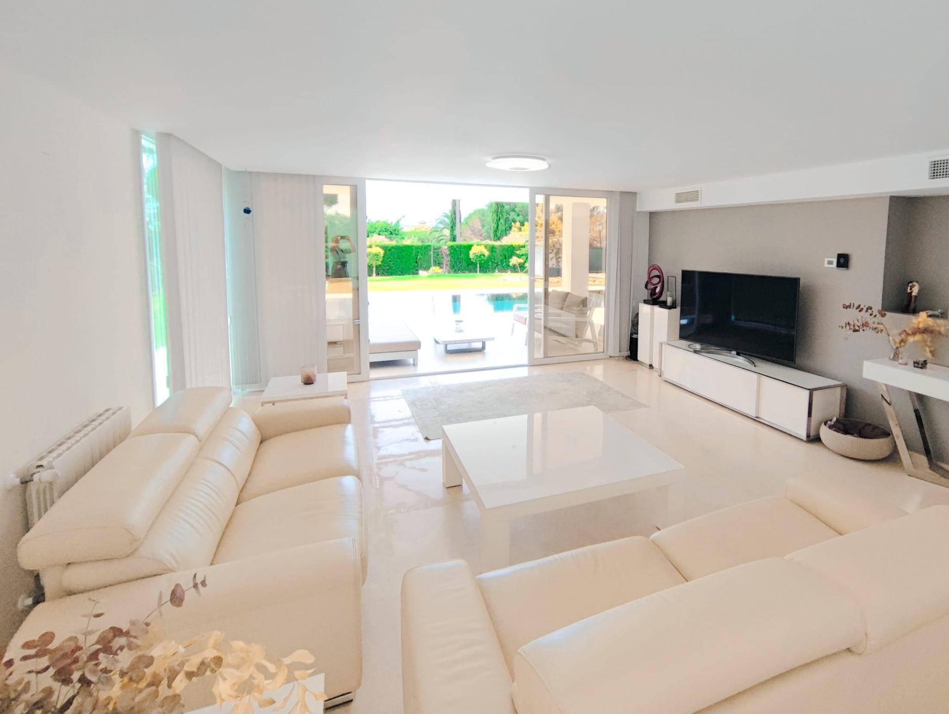 Open-plan living room with floor-to-ceiling glass opening onto the pool and gardens